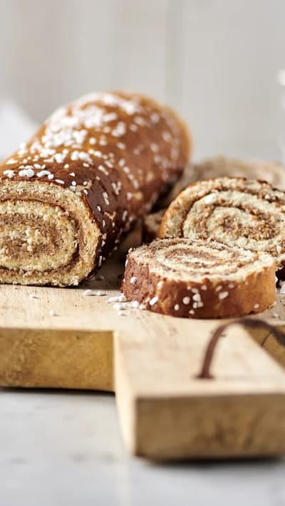 Rulltårta med kanelbullefyllning ligger uppskuren på skärbräda av trä.