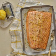 En laxfilé ligger på ett rektangulärt fat bredvid en citron och ett rivjärn på en duk.