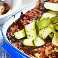 En maträtt med grönsaker serveras i en ugnsform på ett bord med bestick och servetter.