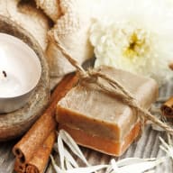 En tvålkaka knuten med snöre ligger bredvid ett tänt värmeljus och kanelstänger.