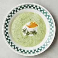 En tallrik med soppa och ett ägg står på en yta bredvid några kvistar.