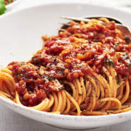 En tallrik med spaghetti och tomatsås står på ett bord bredvid en skål med sallad och ett glas med dryck.