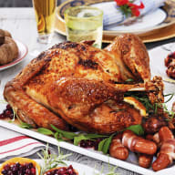 En tillagad hel kyckling på ett fat omgiven av olika maträtter och drycker på ett dukat bord.