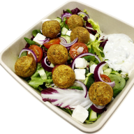 En sallad med falafelbullar, grönsaker och ost serveras i en fyrkantig tallrik med sås på sidan.