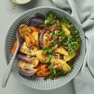En tallrik med tillagad mat står bredvid en skål med sås och en servett på ett bord.