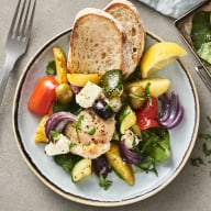 En tallrik med sallad, bröd och gaffel på ett bord.