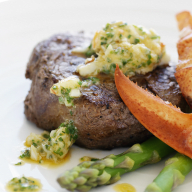 En tallrik innehåller en biff med sås, räkor, sparris och en skaldjurssås.