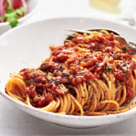 En tallrik med spaghetti och tomatsås står på ett bord bredvid en skål med sallad och ett glas med dryck.