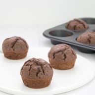 Chokladmuffins ligger på en vit tallrik bredvid en muffinsplåt.