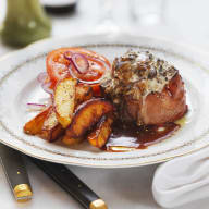 En tallrik med kött, potatis och grönsaker serveras med bestick bredvid.