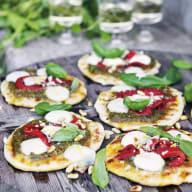 Små pizzor med grönsaker och ost ligger på en träskiva bredvid några glas.