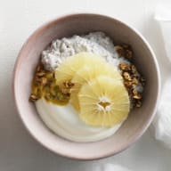 En skål med gröt, citronskivor och granola serveras bredvid en tallrik med mer granola och citronklyftor på en vit yta.