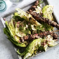 En tallrik med grillspett och sallad står på ett bord bredvid några glasburkar.