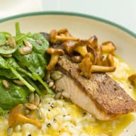 En tallrik innehåller en måltid med kött, sallad och risotto bredvid en gaffel och en servett.