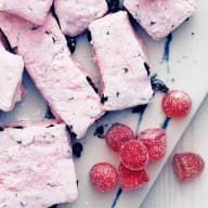 En skärbräda med bitar av marshmallows, några bär och en sax.