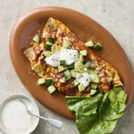 Två burritos ligger på ett tallrik med hackad gurka, gräddfil och salladsblad bredvid en skål med gräddfil.