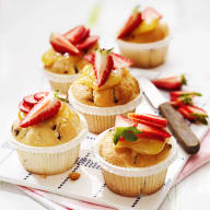 Muffins med jordgubbar ligger på ett vitt underlag bredvid en kniv.