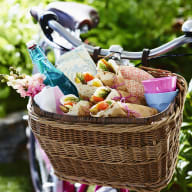 En cykel med en korg full av picknickmat och dryck står i en grön utomhusmiljö.