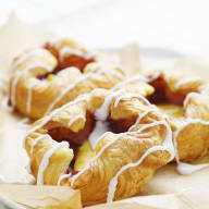 En tallrik med bakverk som ser ut som croissanter, täckta med ett vitt glasyrliknande överdrag.