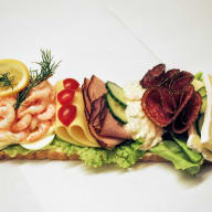 En smörgås med räkor, skinka, grönsaker och ost ligger på ett bord.