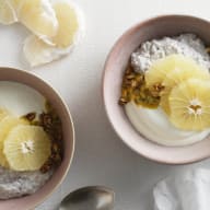 En skål med gröt, citronskivor och granola serveras bredvid en tallrik med mer granola och citronklyftor på en vit yta.