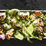 En sallad med grönsaker och kött serveras på ett rektangulärt fat mot en mörk bakgrund.