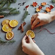Händer trär på torkade apelsinskivor på en silvertråd