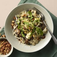 En skål med risotto med stekt svamp står på en duk bredvid en skål med mandlar.