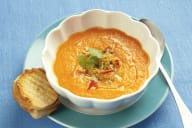 En skål med soppa står på en tallrik tillsammans med en brödskiva.