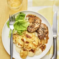 Tallrik med potatisgratäng och kryddade köttbitar, serverad med sallad och bestick.