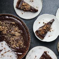 En chokladtårta med nötter serveras i bitar på flera små tallrikar bredvid en hel tårta på ett mörkt underlag.