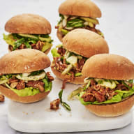 Fem små hamburgare med sallad och kött ligger på en vit serveringsbricka bredvid en skål.