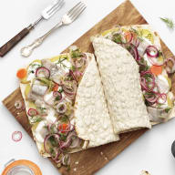 En tallrik med tortillabröd och sallad står på en skärbräda tillsammans med bestick och små skålar med tillbehör.