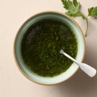 En skål med gemolata och en sked står på ett underlag.