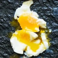 Kokt ägg med mjukkokt vita och helt rinnande gula mot svart botten,.