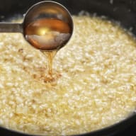 En sked häller honung över en skål med risotto.
