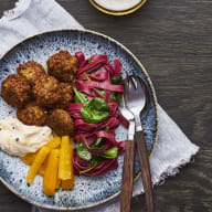 En tallrik med köttbullar, grönsaker och bestick står på en duk på ett träbord.