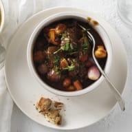 En tallrik med gryta och en skål med potatismos står på ett bord bredvid ett glas vatten och en servett.