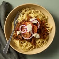 En tallrik med spaghetti och köttfärssås står på en duk.