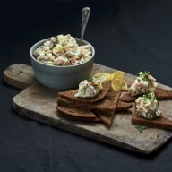 En tallrik med sallad och brödskivor står på en träskärbräda bredvid en skål med mer sallad.