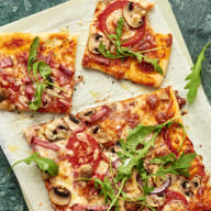 Pizzabitar med pålägg av skinka, svamp och rucola ligger på en skärbräda.