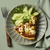 En bit paj med oliver och sallad ligger på en tallrik bredvid en gaffel.