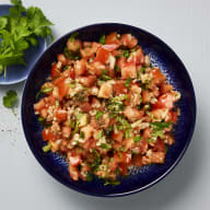 En skål med tomatsalsa med örter står på ett underlag.