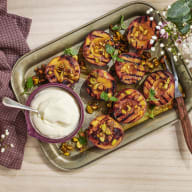 En tallrik med grillade frukter serveras bredvid en skål med sås och dekorativa växter på ett bord.