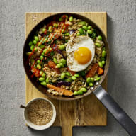 Fried rice i en stekpanna, på det stekta riset ligger ett stekt ägg, bredvid står en skål med rostade sesamfrön.