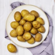 Kokad färskpotatis som ligger i en skål, skålen står på en lila handduk.