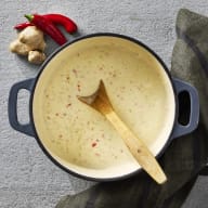 Kokosbuljong i en kastrull, bredvid kastullen ligger chili och vitlök.