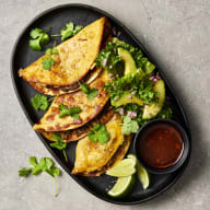 Birria tacos ligger på en fat tillsammans med avokadosallad och limeklyftor.