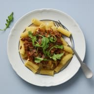 En tallrik med pasta med en paprikagryta med pulled pork som står på ett underlag.