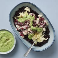 En skål med svart ris, coleslaw och  bön- och fetaröra med sås som står på ett underlag.